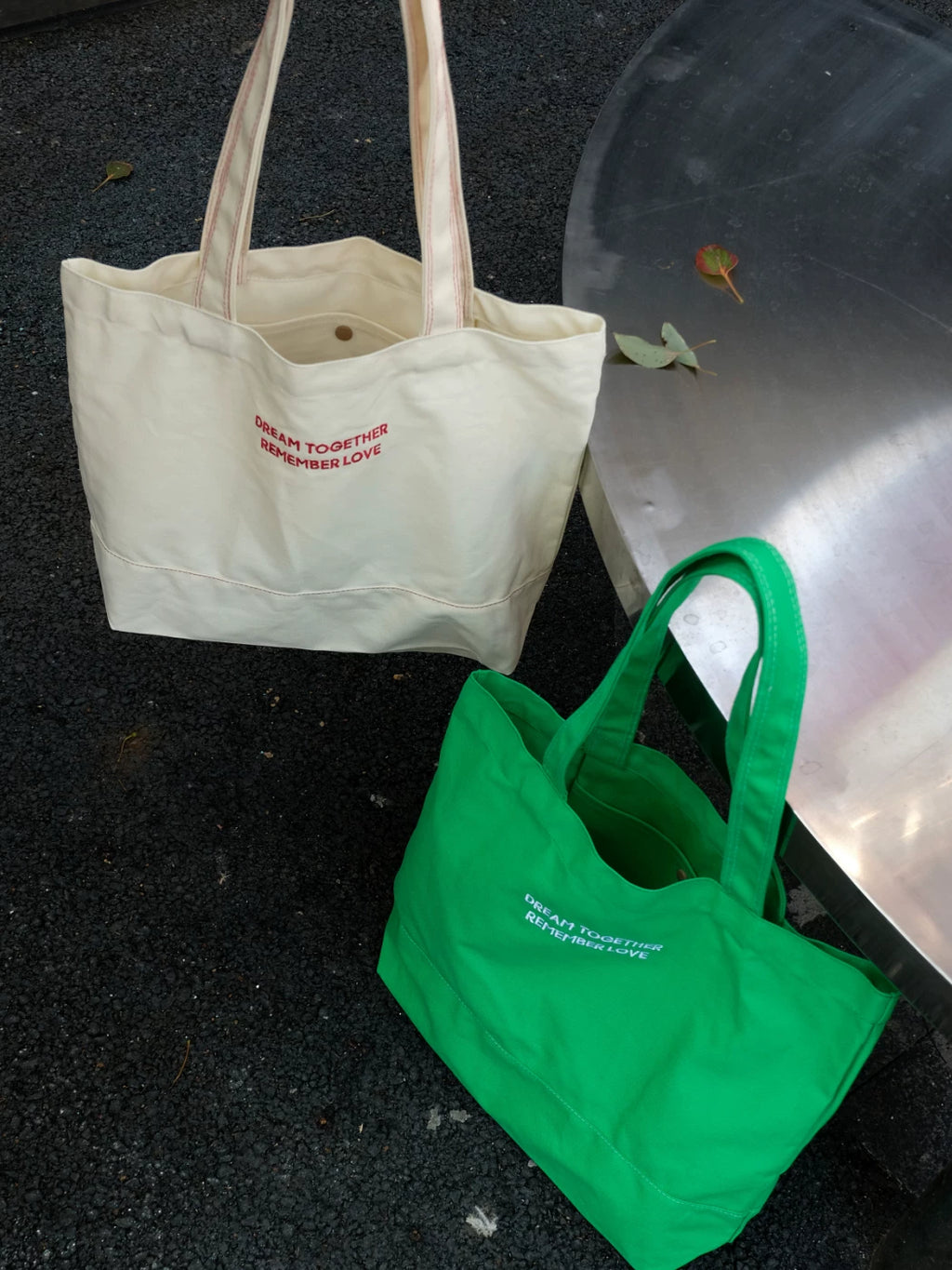 Beige tote bag and green tote bag on a dark surface