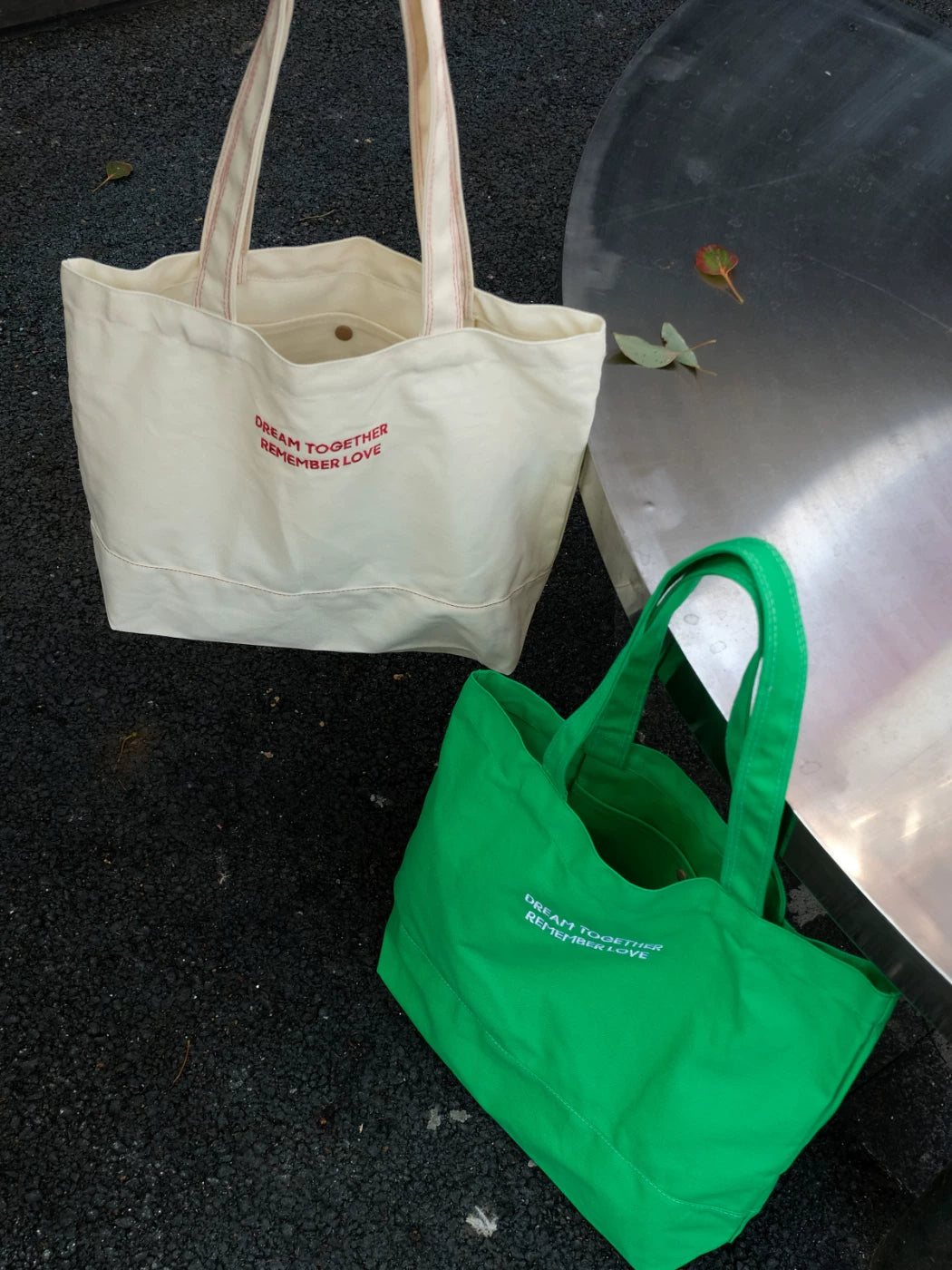 Beige tote bag and green tote bag on a dark surface