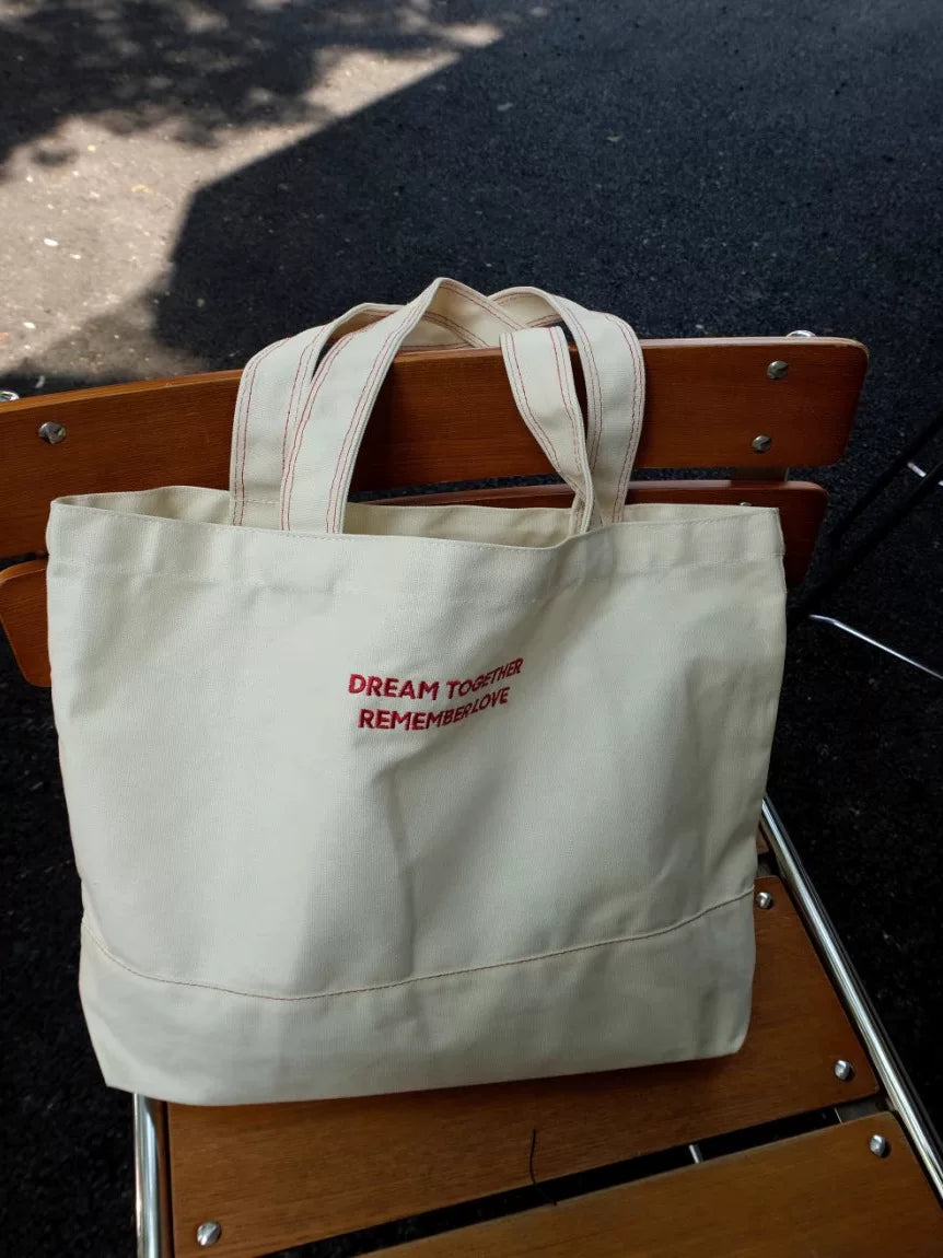 Beige tote bag with red text on a wooden chair outdoors