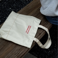 White tote bag with red text on a wooden bench