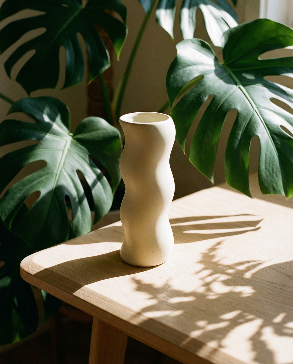 White vase on a wooden table with green leaves in the background